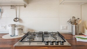 A kitchen with a gas stove, two stainless steel containers, a hanging pot rack, and a utensil holder.