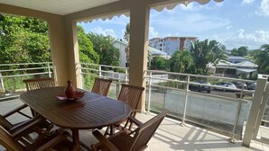 Ein überdachter Balkon mit Holztisch und -stühlen, der einen Blick auf eine Wohngegend mit Häusern und parkenden Autos bietet.