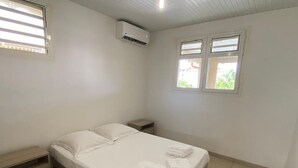 Ein helles, sauberes Schlafzimmer mit einem Einzelbett, einem Nachttisch, einem kleinen Tisch und einem Fenster mit Jalousien.