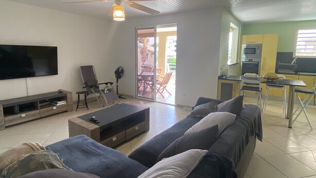 Ein Wohnzimmer mit einer Couch, einem Fernseher, einem Deckenventilator und einem Essbereich mit Stühlen und einem Tisch.