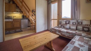 A compact living space with a kitchen, a wooden staircase, a sofa with patterned cushions, and a wooden table. - Valmorel, 2 rooms + mezzanine, 6 people, simple, pets, skiers (Valmorel)