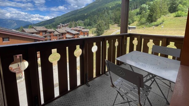 A balcony with a table and chairs, overlooking a mountainous area with buildings in the distance. - Valmorel, 2 rooms + mezzanine, 6 people, simple, pets, skiers (Valmorel)