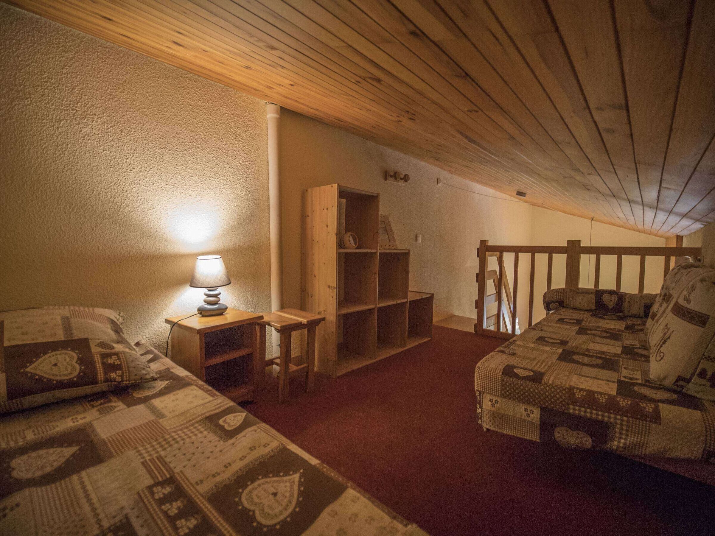 Une chambre mansardée chaleureuse, avec deux lits, une bibliothèque en bois et une lampe.