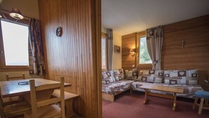 A cozy cabin interior with a wooden dining table, chairs, a sofa with patterned cushions, and a red carpet. - Valmorel, 2 rooms + mezzanine, 6 people, simple, pets, skiers (Valmorel)