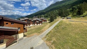 A mountain lodge with multiple wooden buildings, a gravel path, and a view of a forested mountain range. - Valmorel, 2 rooms + mezzanine, 6 people, simple, pets, skiers (Valmorel)