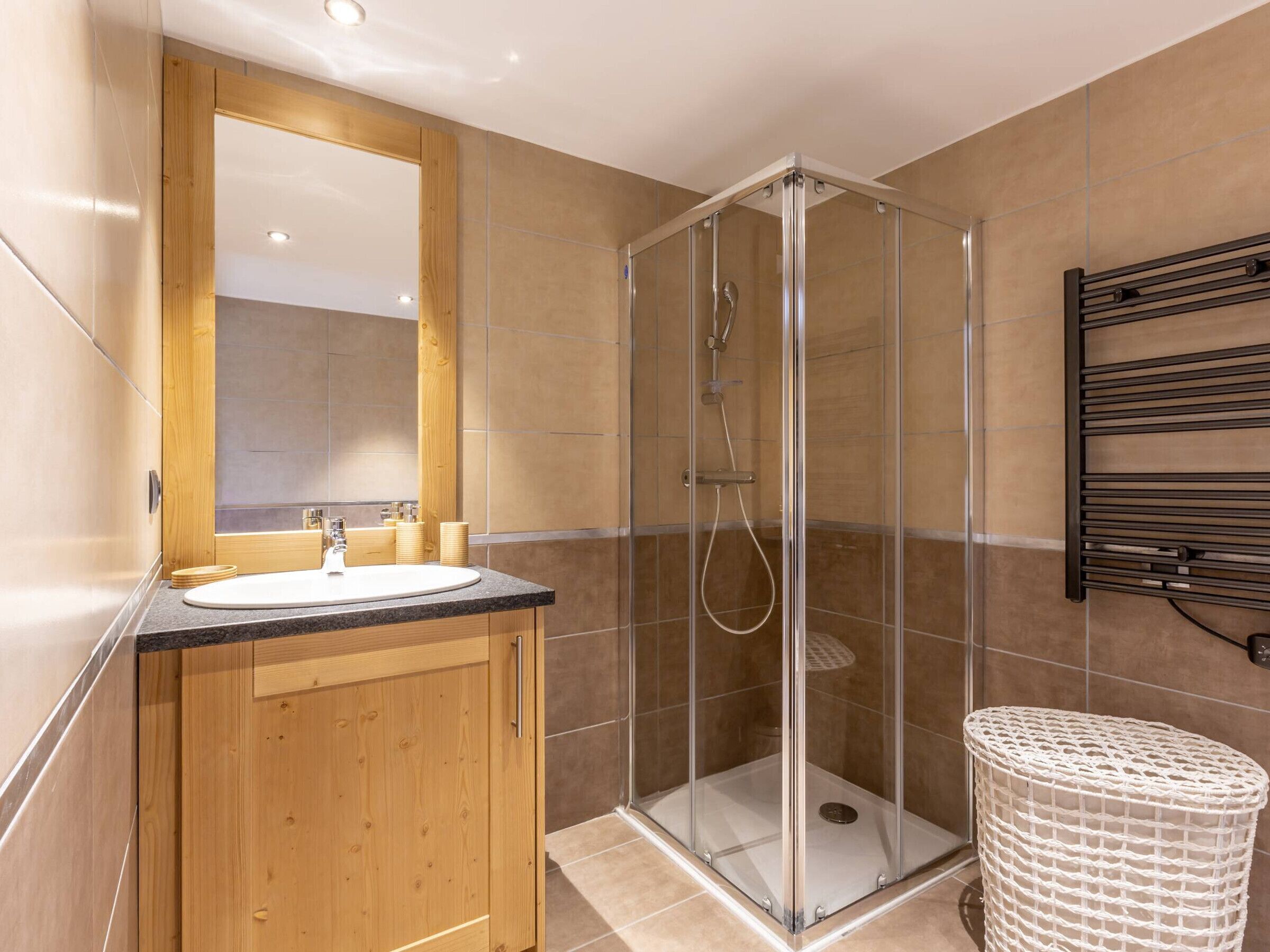 Een moderne badkamer met een houten wastafelmeubel, een douchecabine met glazen wanden en een handdoekhouder.