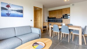 A modern living room with a grey sofa, a wooden dining table with chairs, and a kitchen with wooden cabinets and a black countertop. - 3-room apartment with parking, Wi-Fi, pets allowed, 50m from slopes in Valmorel (Valmorel)