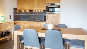 A modern kitchen with wooden cabinets, a built-in oven, and a dining area with a wooden table and grey upholstered chairs. - 3-room apartment with parking, Wi-Fi, pets allowed, 50m from slopes in Valmorel (Valmorel)