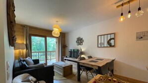 Un salón acogedor con sofá, mesa de comedor y televisor. Se aprecia una ventana con vistas a zonas verdes.