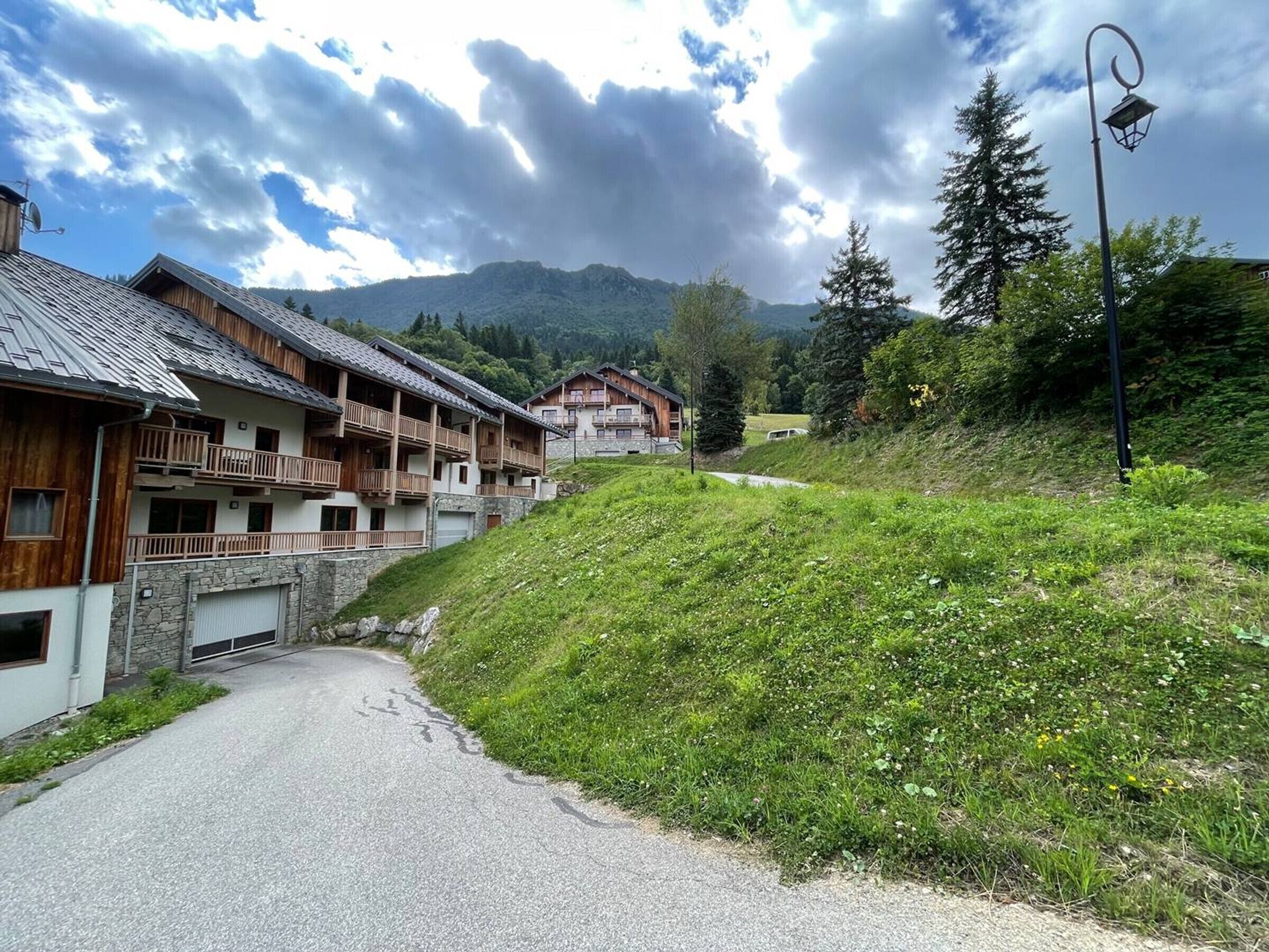 A row of wooden buildings with balconies, a paved road, and a mountain in the background.