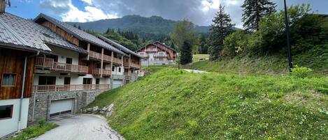 A row of wooden buildings with balconies, a paved road, and a mountain in the background.