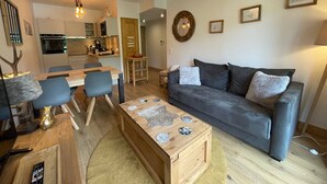 Una sala de estar moderna con un sofá gris, una mesa de centro de madera y un comedor con una mesa y sillas de madera.