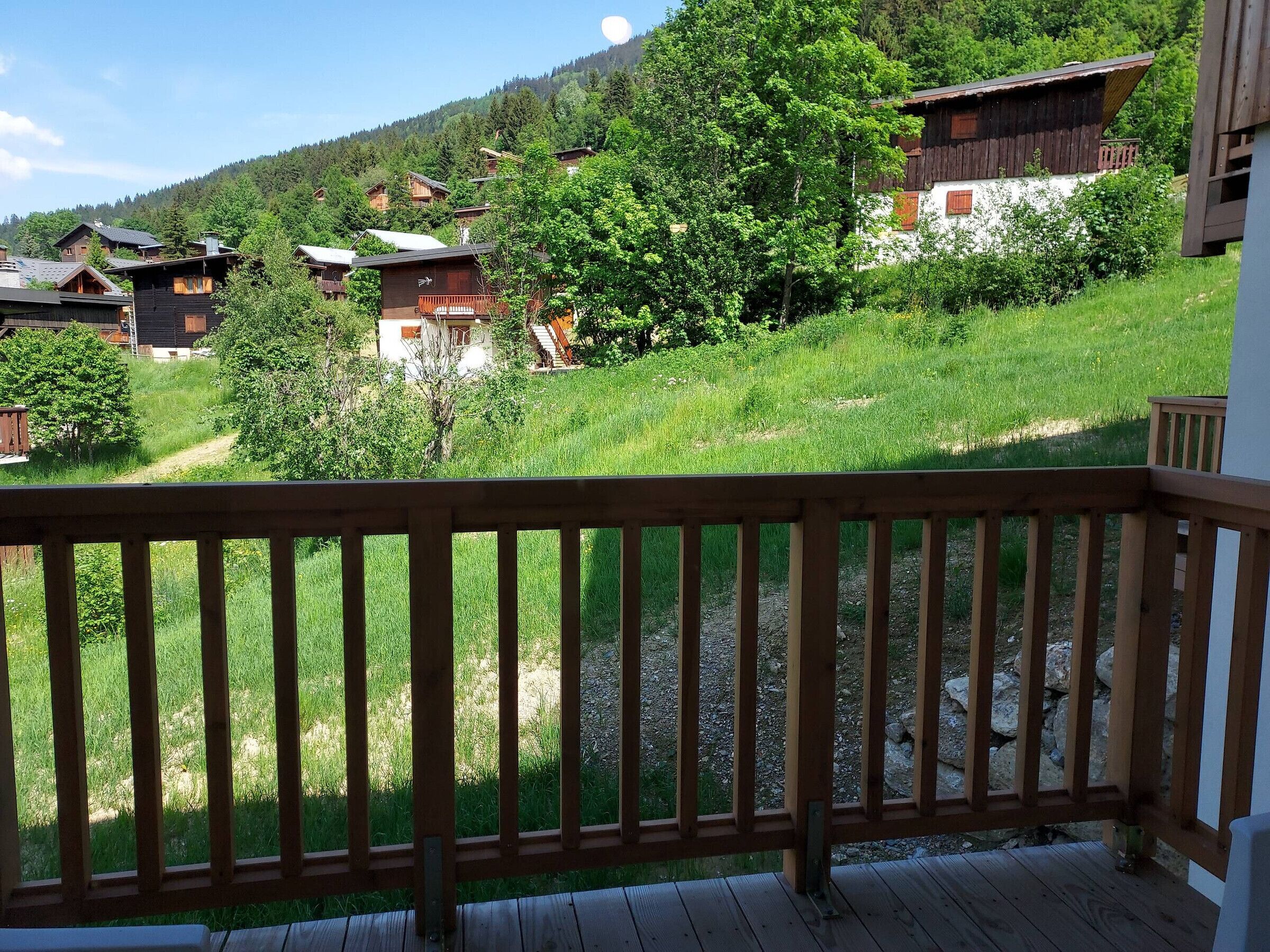 A wooden deck with a view of a mountainous area, featuring rustic cabins and lush greenery.