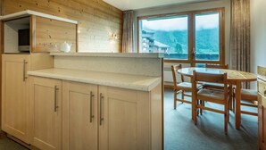 A kitchen with wooden cabinets and a window overlooking a mountainous landscape. - Cozy 2-room apartment in Valmorel, 50m from slopes, pets allowed (Valmorel)
