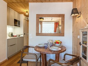 A wooden-paneled room with a dining table set for two, a kitchen area with modern appliances, and a large mirror on the wall.