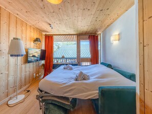 A room with a bed, a television, a window with curtains, and a wooden ceiling.