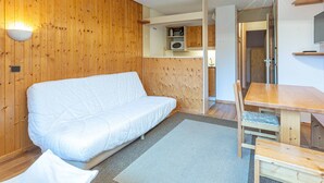 Une pièce chaleureuse avec un mur en bois, un canapé blanc, une table à manger avec des chaises et un luminaire au plafond.