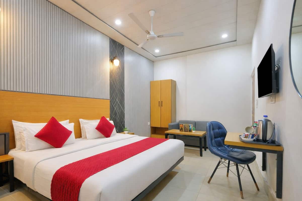A hotel room with a large bed, a desk with a chair, a wardrobe, and a flat-screen TV mounted on the wall.