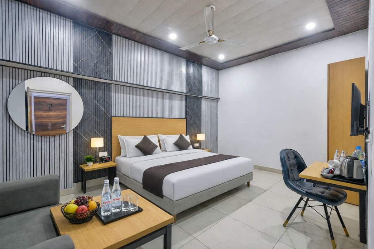 A modern hotel room with a bed, bedside tables, a desk, a chair, and a round mirror.
