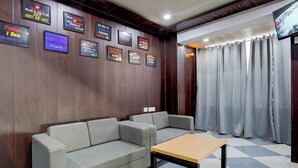 A hotel lobby with a grey sofa, a wooden table, and a television mounted on the wall. - Hotel Downtown by Quadis - Sector 15 Noida (Noida)