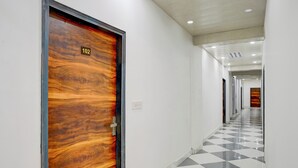 A hallway with a checkered floor, a wooden door with a number, and a light switch on the wall. - Hotel Downtown by Quadis - Sector 15 Noida (Noida)