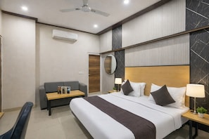 A hotel room with a bed, a sofa, a desk, and a ceiling fan. - Hotel Downtown by Quadis - Sector 15 Noida (Noida)