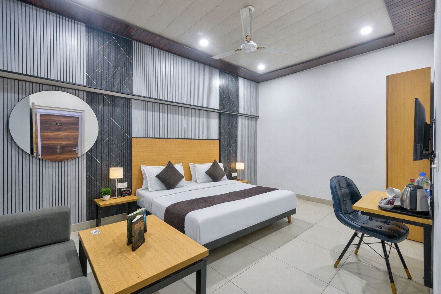 A hotel room with a bed, bedside tables, a desk, a chair, a TV, and a ceiling fan.