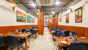 A restaurant with wooden paneling, marble flooring, and framed artwork on the walls. Tables are set with plates, glasses, and cutlery. - Hotel Downtown by Quadis - Sector 15 Noida (Noida)