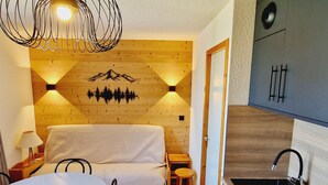 Une pièce chaleureuse avec un mur en bois, un canapé, une table à manger et un coin cuisine équipé d’un évier et de placards.