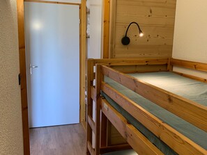 Ein Holzbett mit Etagen, einem Kopfteil, einer weißen Tür und einer Wandleuchte.