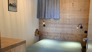 Une chambre à coucher avec une tête de lit en bois, un lit recouvert d’une couvre-lit bleue, deux lampes de lecture fixées au mur, une table de chevet en bois et un tableau encadré accroché au mur.