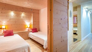 Ein Zimmer in einer Holzhütte mit zwei Betten, jedes mit einem roten Kissen und weißer Bettwäsche. An beiden Seiten der Betten befinden sich Wandlampen.