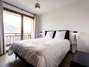 Een slaapkamer met een groot bed, twee bedlampen, uitzicht op bergen door een raam en een balkon.