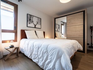 Een slaapkamer met een bed, nachtkastje, lamp, raam en spiegel.