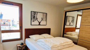 A neatly made bed with white linens, a small bedside table with a lamp, and two framed pictures on the wall. - Beautiful apartment in Plagne Montalbert, near slopes with wifi and parking (La Plagne Montalbert)