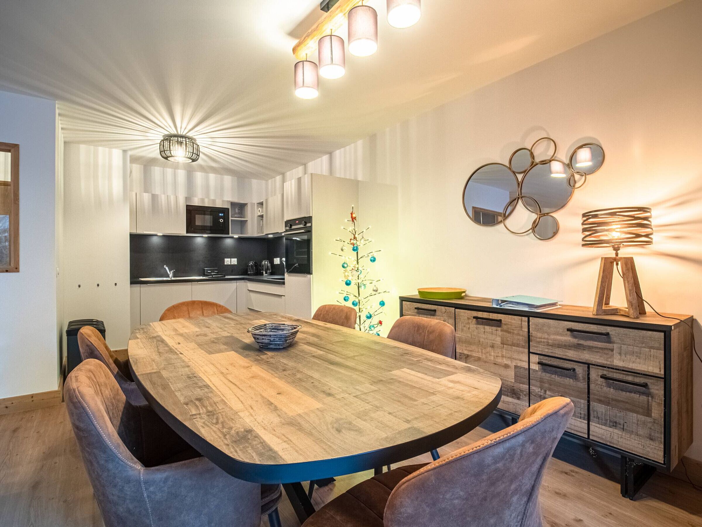 A modern kitchen with a dining area, featuring a wooden table, chairs, and a decorative wall piece.