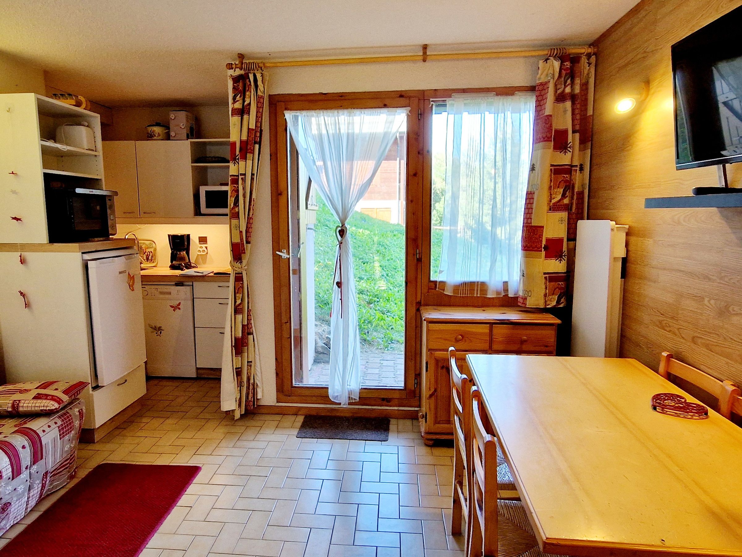 A compact kitchen with a dining area, wooden cabinets, a microwave, and a television.