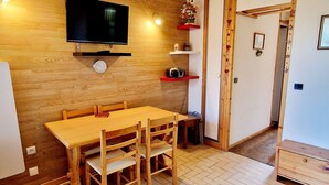 Een houten eettafel met stoelen, een flatscreen televisie aan de wand en een klok.