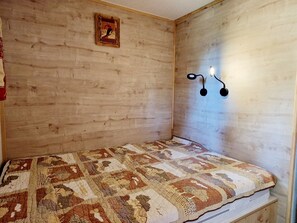 Um quarto pequeno e acolhedor com parede de madeira, colcha acolchoada e luminária fixada na parede.