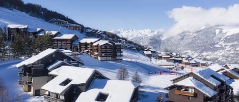 A snow-covered mountain resort with wooden buildings, ski slopes, and a clear blue sky.