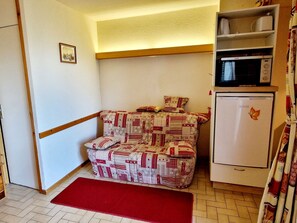 A corner room with a patterned sofa, a microwave, and a refrigerator.