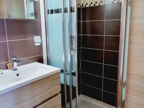 A modern bathroom with a glass shower enclosure, a white sink, and dark tiled walls.