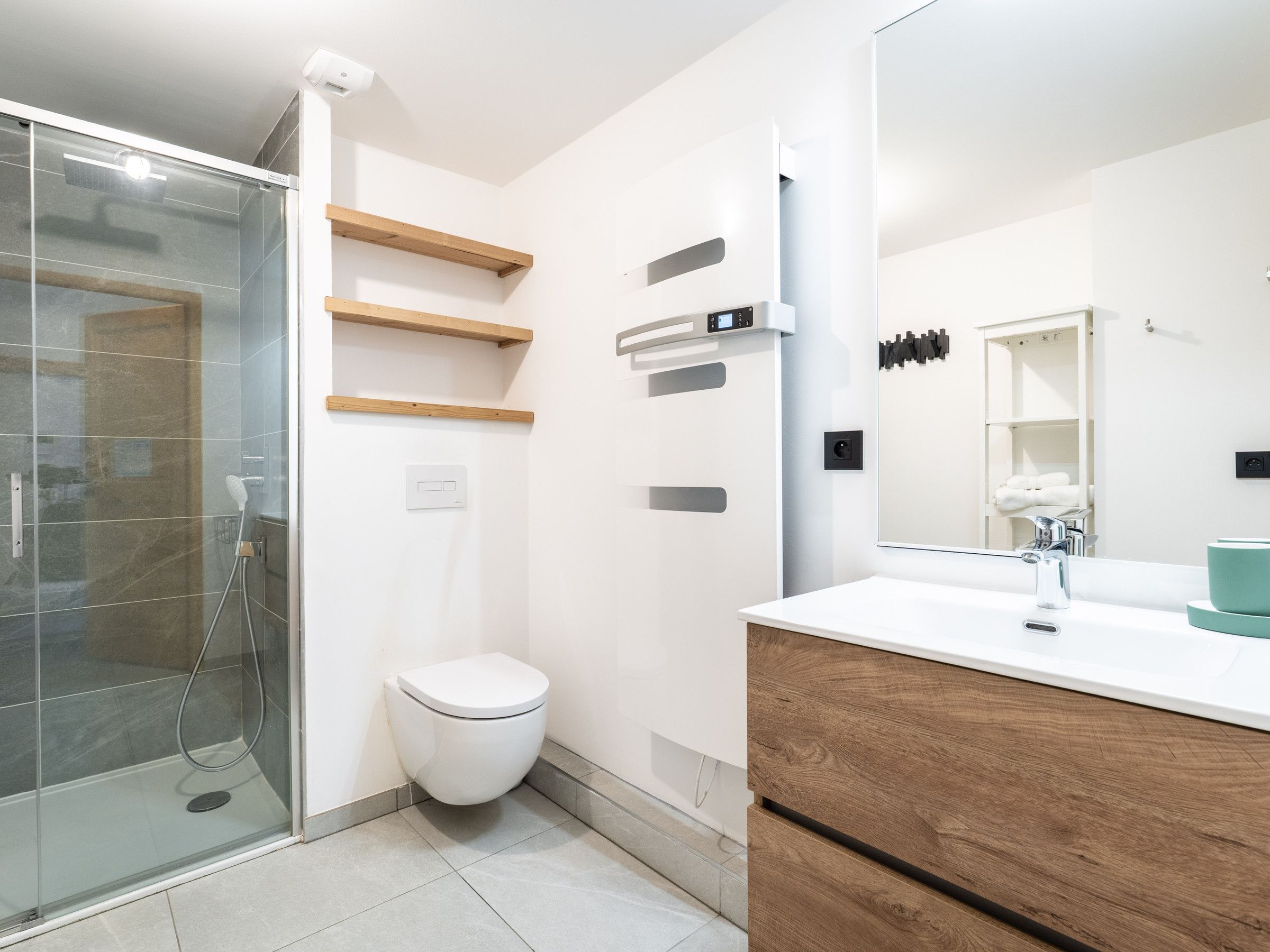 Een moderne badkamer met een douchecabine van glas, een wit toilet en een houten wastafelmeubel met spiegel.