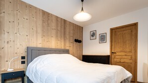 A bedroom with a wooden wall, a bed, a nightstand, a dresser, and a door. - Cozy 2-room apartment in Plagne Montalbert, close to slopes and shops, with garage and wifi (La Plagne Montalbert)