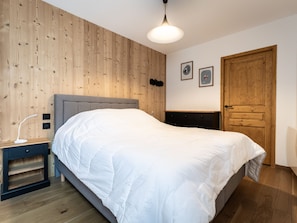 Una camera da letto con un muro in legno, un letto, un comodino, una cassettiera e una porta.