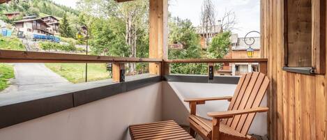 A wooden balcony with a chair and table, overlooking a residential area with houses and trees.