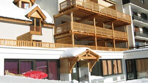 Ein mehrstöckiges Gebäude mit hölzernen Balkonen und einer Skipiste im Vordergrund.