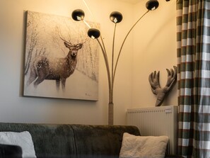 A living room with a sofa, a deer painting, a deer antler decoration, and a floor lamp.