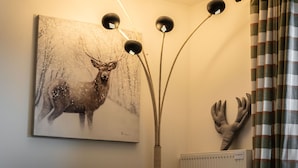 Een woonkamer met een bank, een hert schilderij, een decoratie van hertengewei en een vloerlamp.