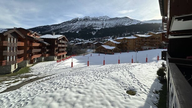 Et skisportssted dækket af sne med træhuse og et bjerg i baggrunden.
